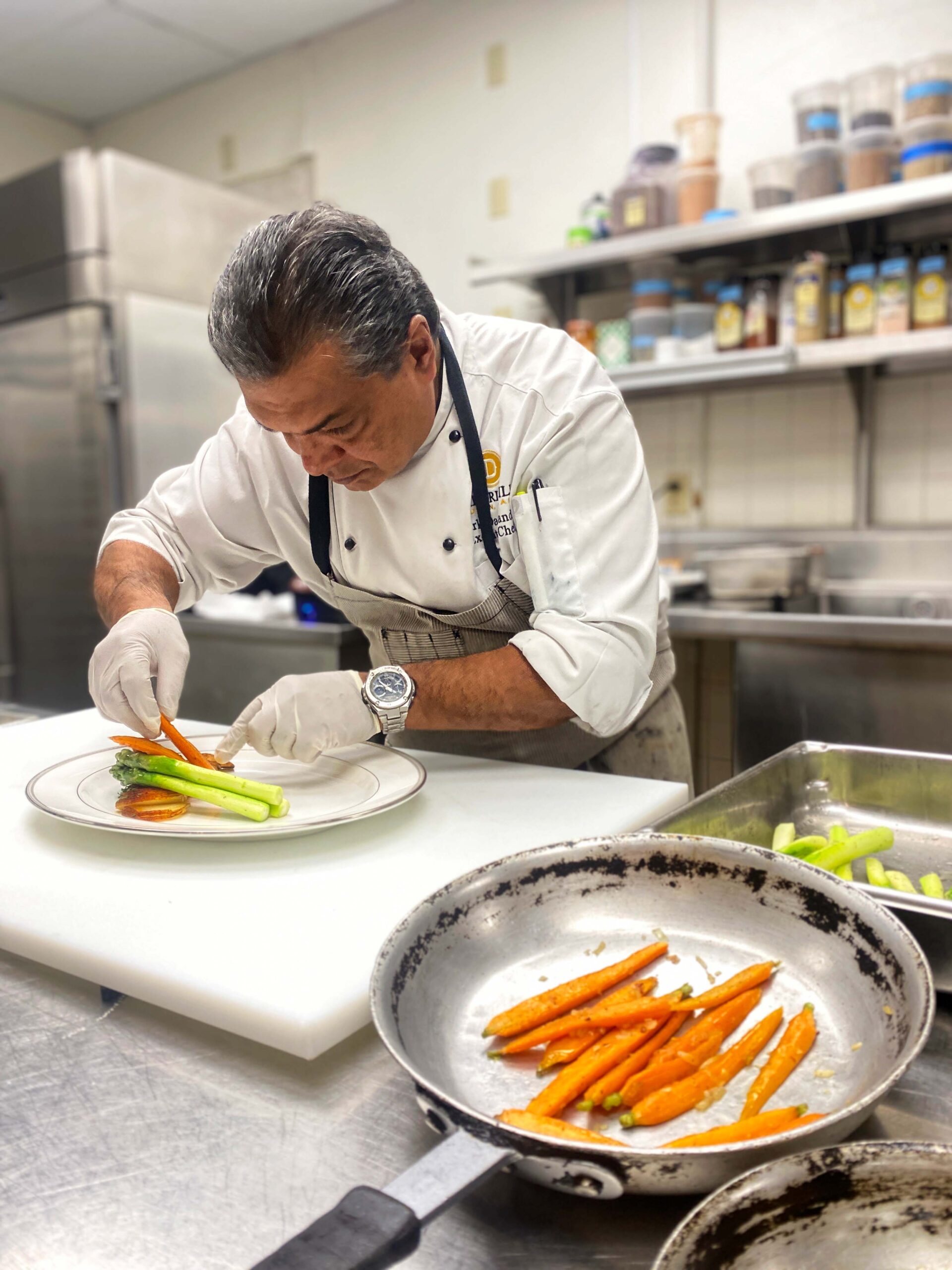 Chef Mark of The Driskill Hotel plating carrots and asparagus in the kitchen.