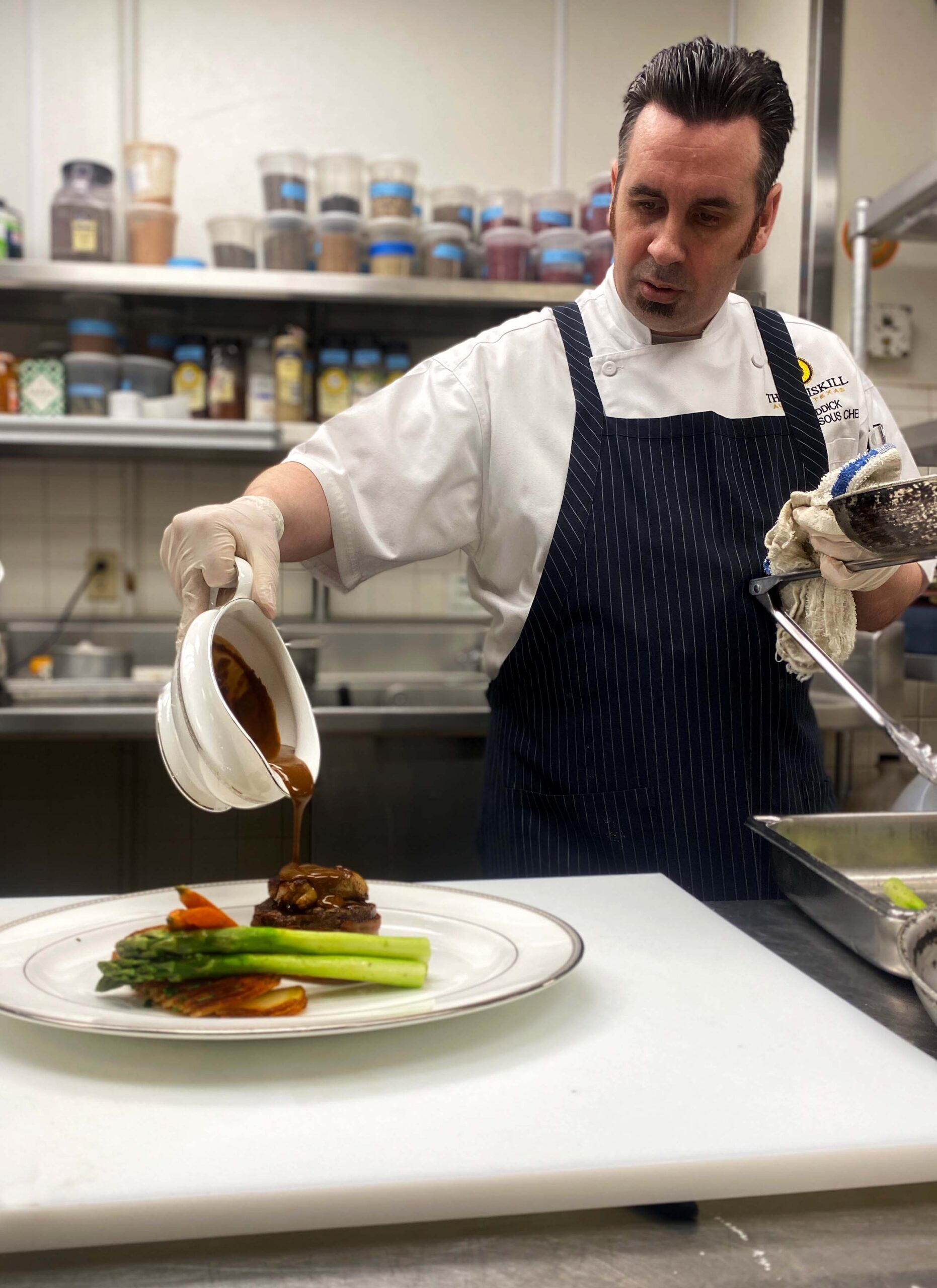 Sous Chef Iain pouring sauce over plated steak.