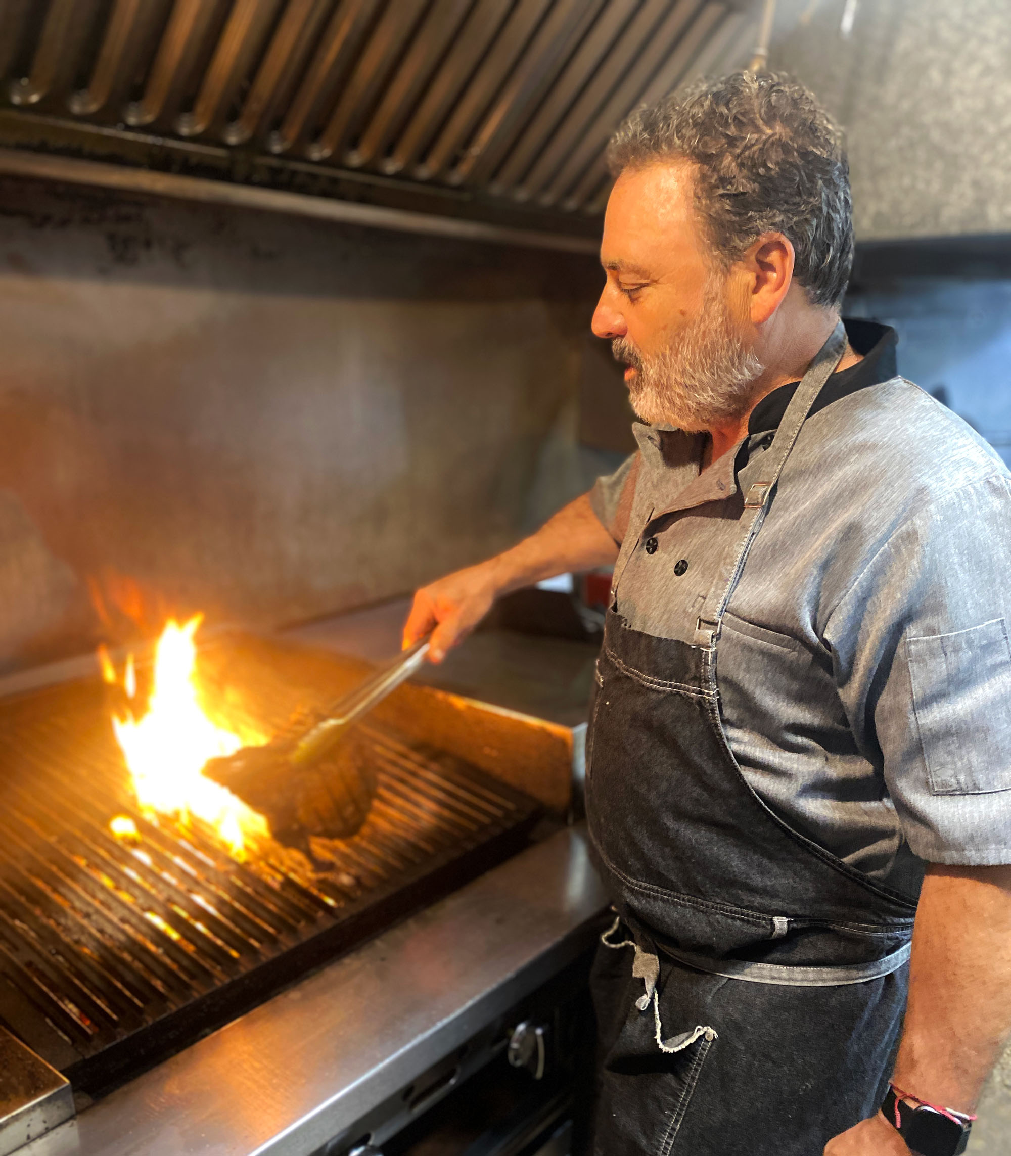 Chef Christian Mertens grills a bone-in steak over an open flame.