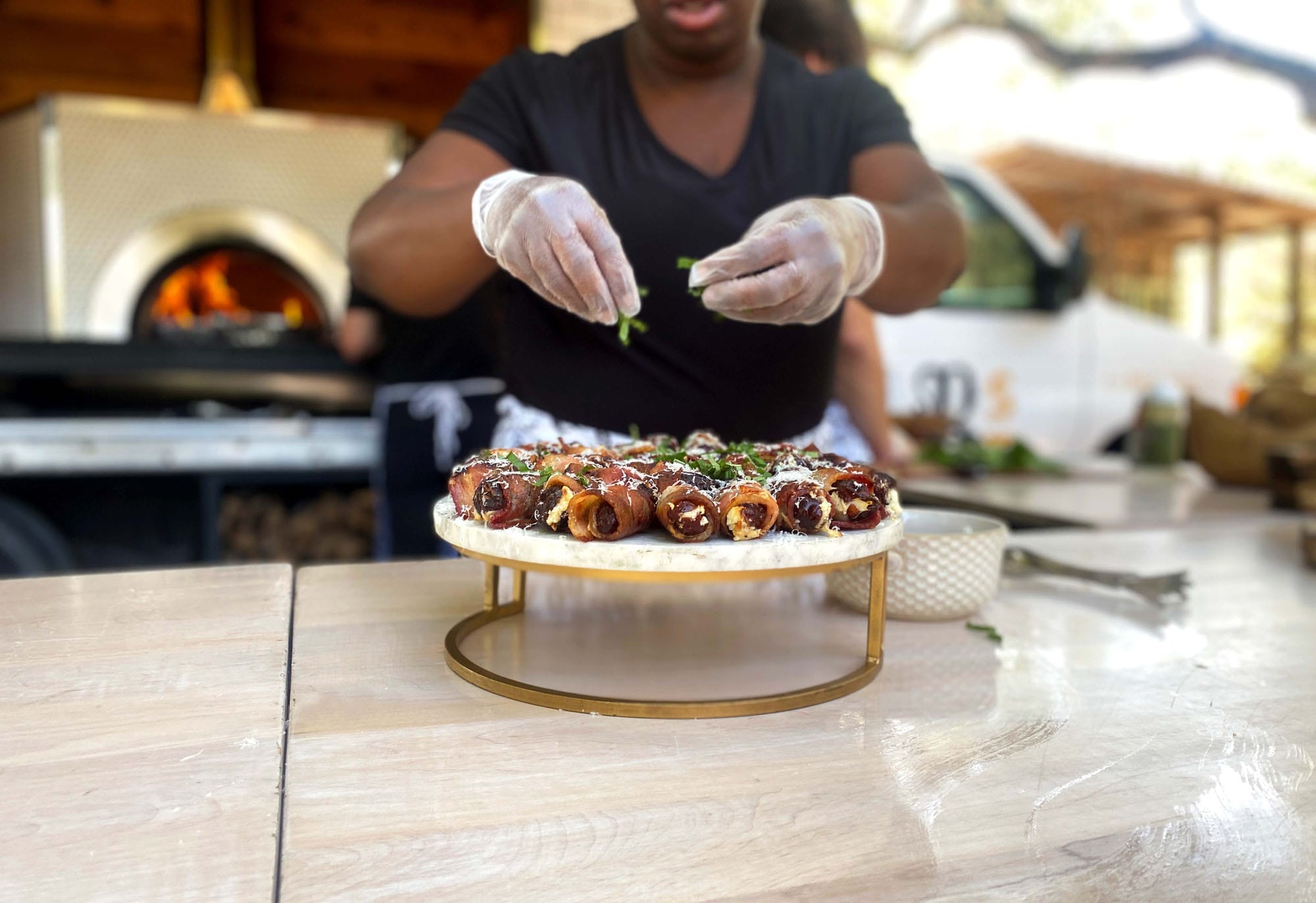 A woman garnishing a plate of bacon wrapped dates.
