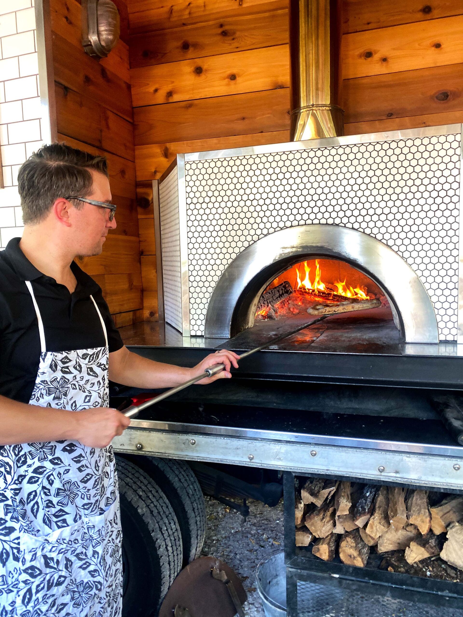 Rocky Shanower of Bahler Street pizza sliding a pizza into the wood fire oven.