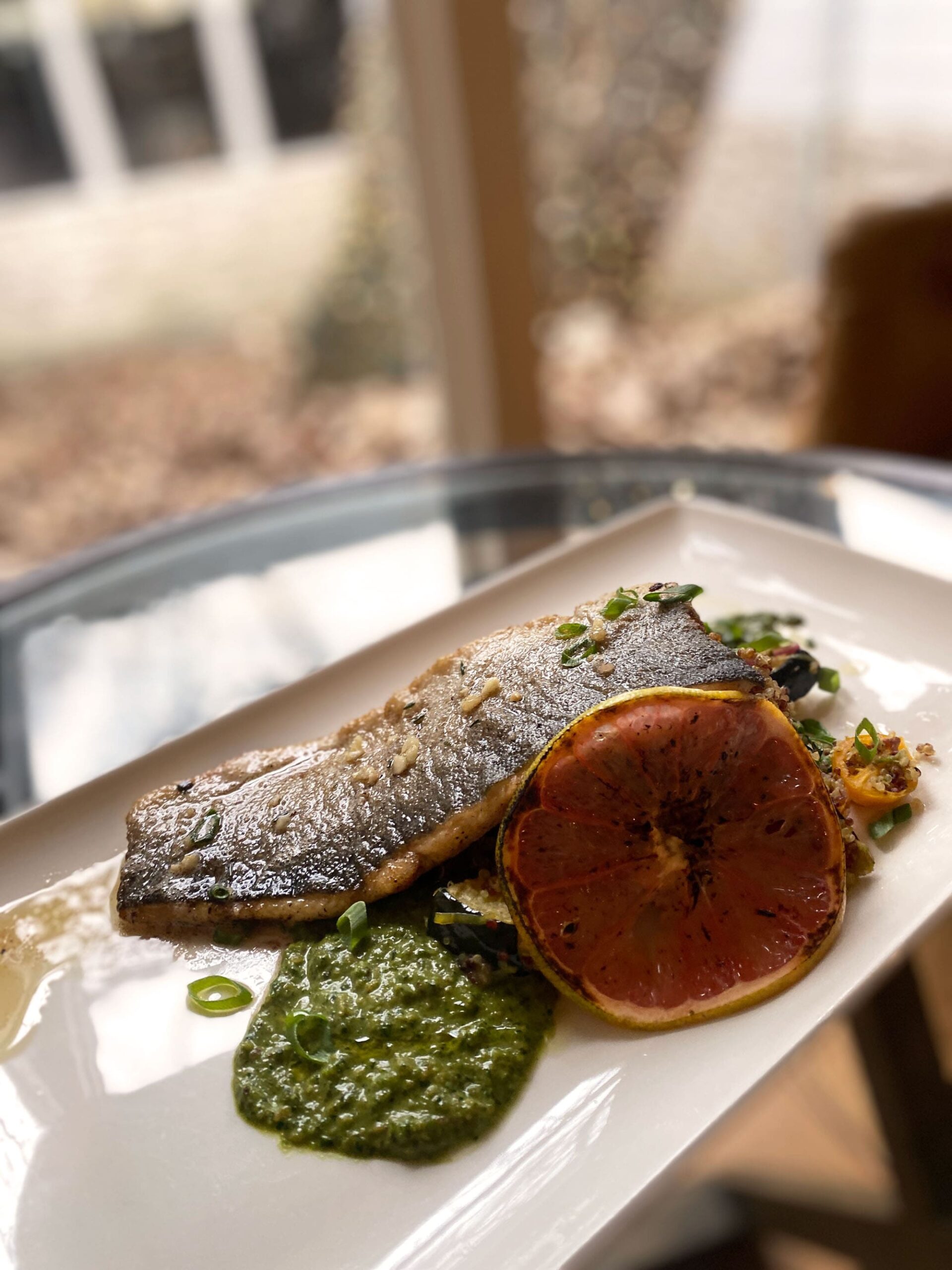 Trout and grapefruit on a white rectangular dish in front of a window.