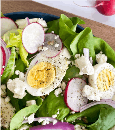 Butter lettuce salad in blue bowl with hard boiled eggs, onion, radishes and feta cheese.