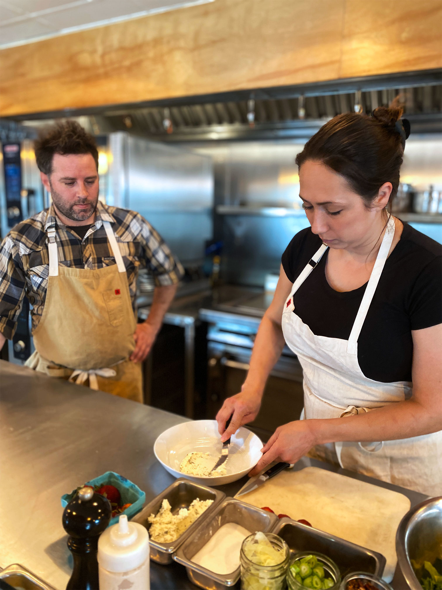 Chef Sarah Heard spreads butter onto a white plate while Chef Nathan Lemley watches.