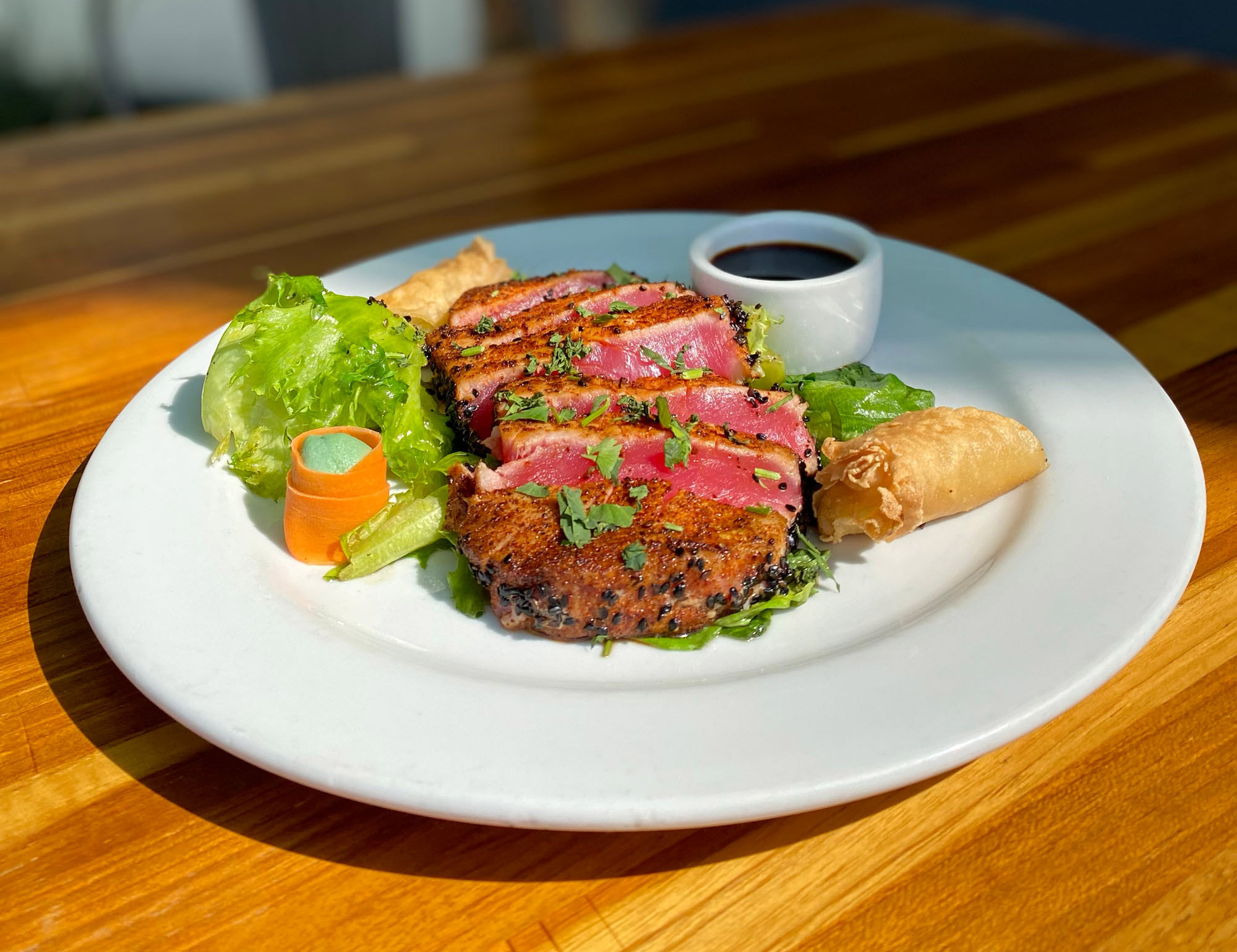 Seared ahi tuna, a spring roll, and TrueHarvest Crispy Leaf sit on a white plate on a wooden table.