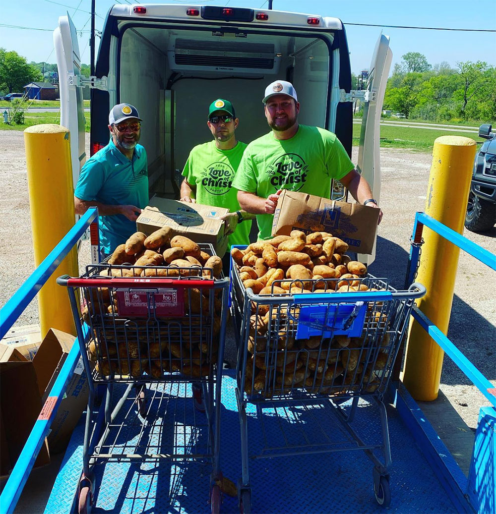 Three men standing in front of donated potatoes for a food pantry donation.